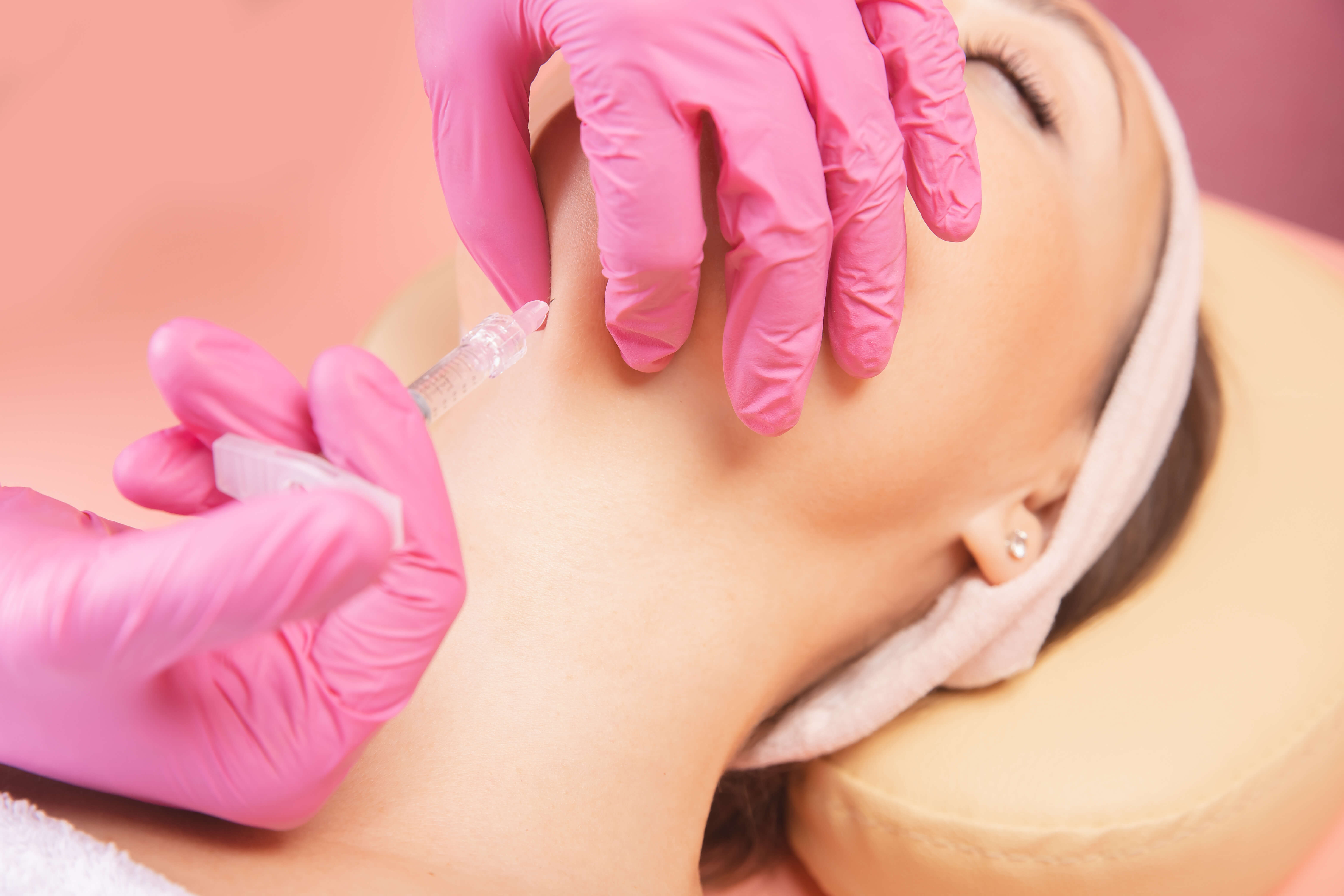 Person receiving a facial treatment with pink gloves on a pink background