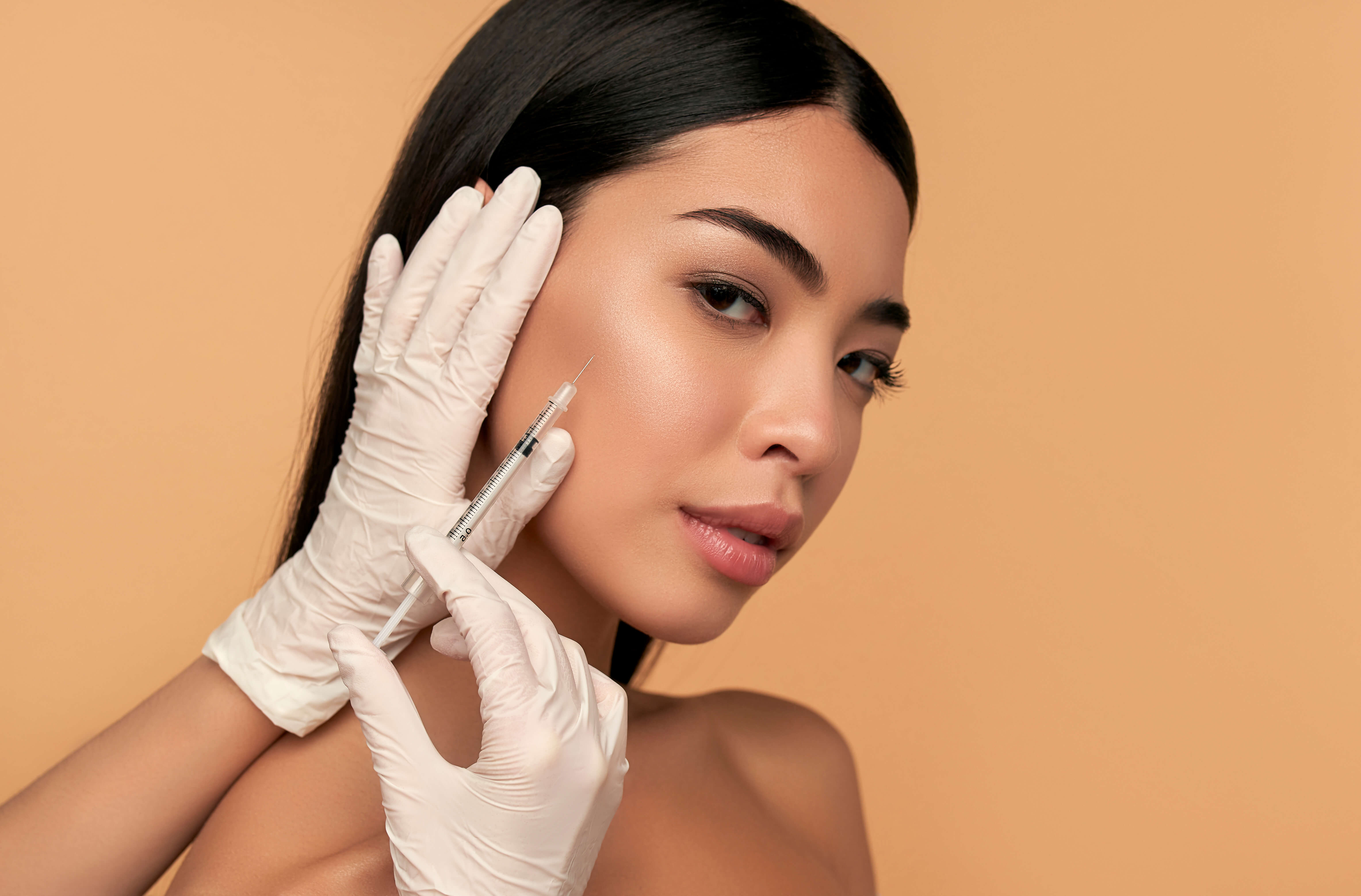 Woman receiving a cosmetic filler injection with gloves on a beige background