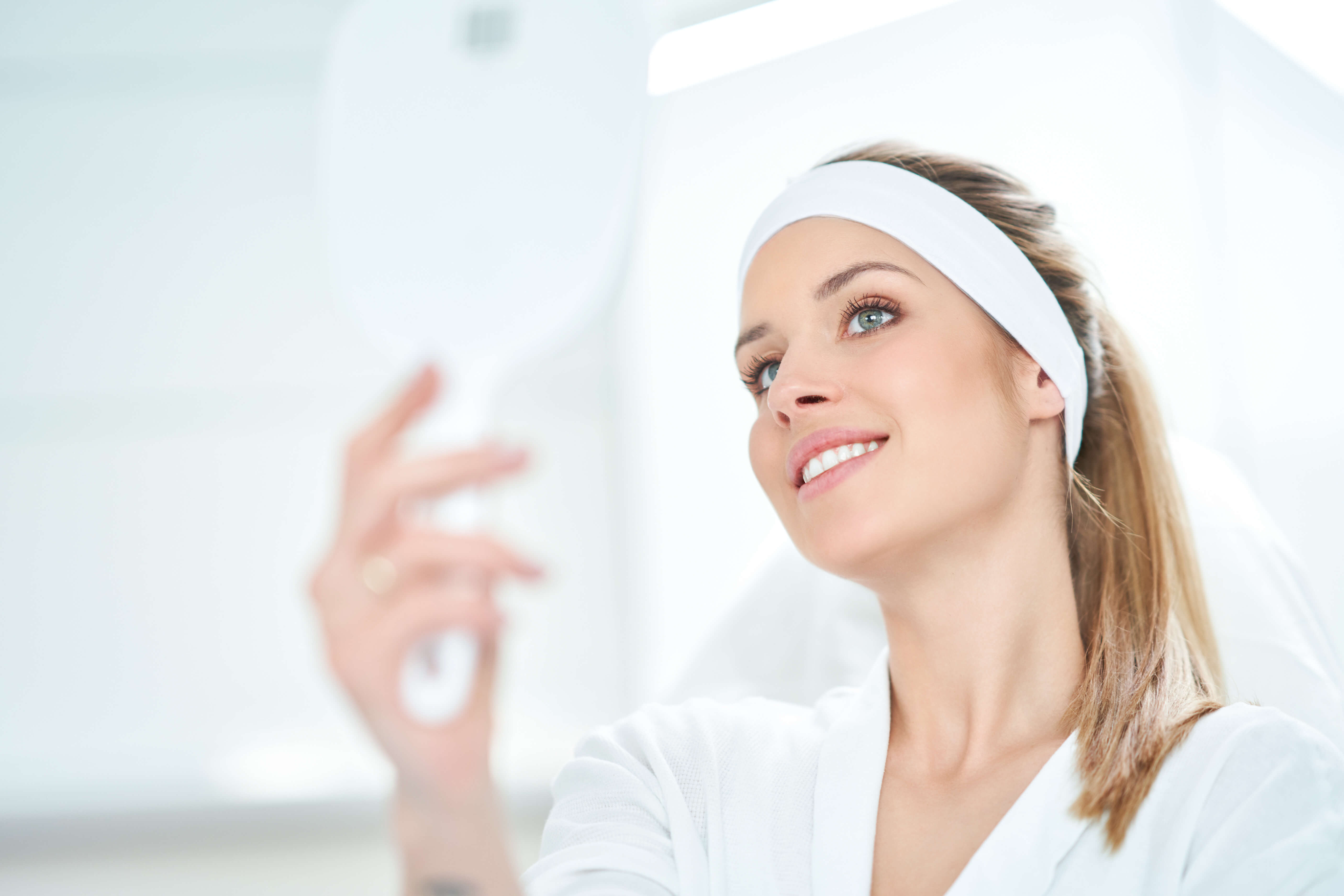 Woman wearing a white headband and robe, holding a mirror.