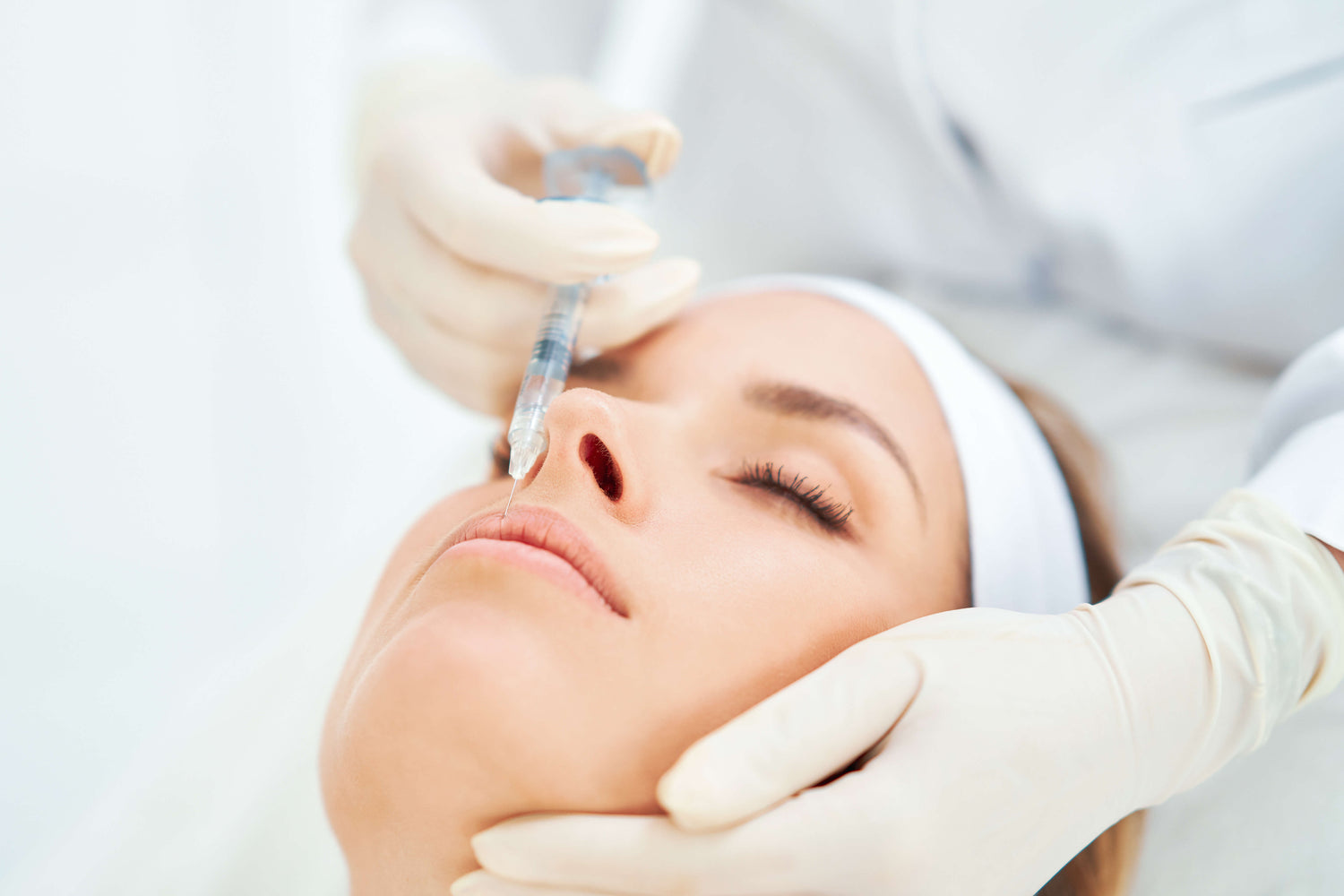Person receiving a lip filler injection with medical gloves on a white background